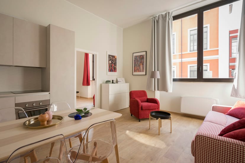 Pièce de vie ouverte, coin repas, fauteuil rouge et fenêtre sur rue
