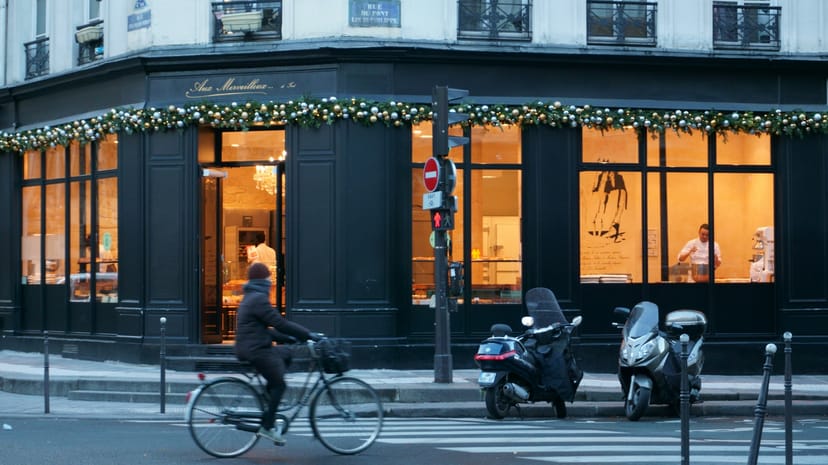 Devanture éclairée d’un café au pied d’un immeuble parisien, un cycliste passe